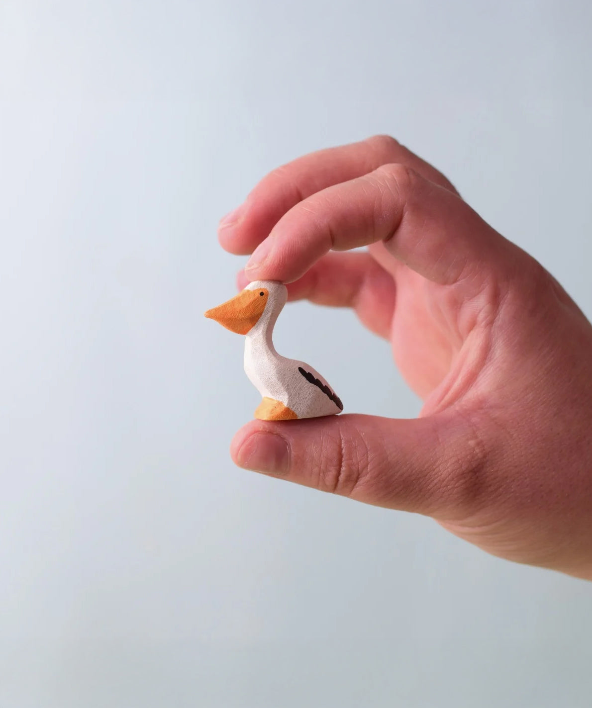 Bumbu Toys Wooden Pelican Chick, being held in an adult's hand.