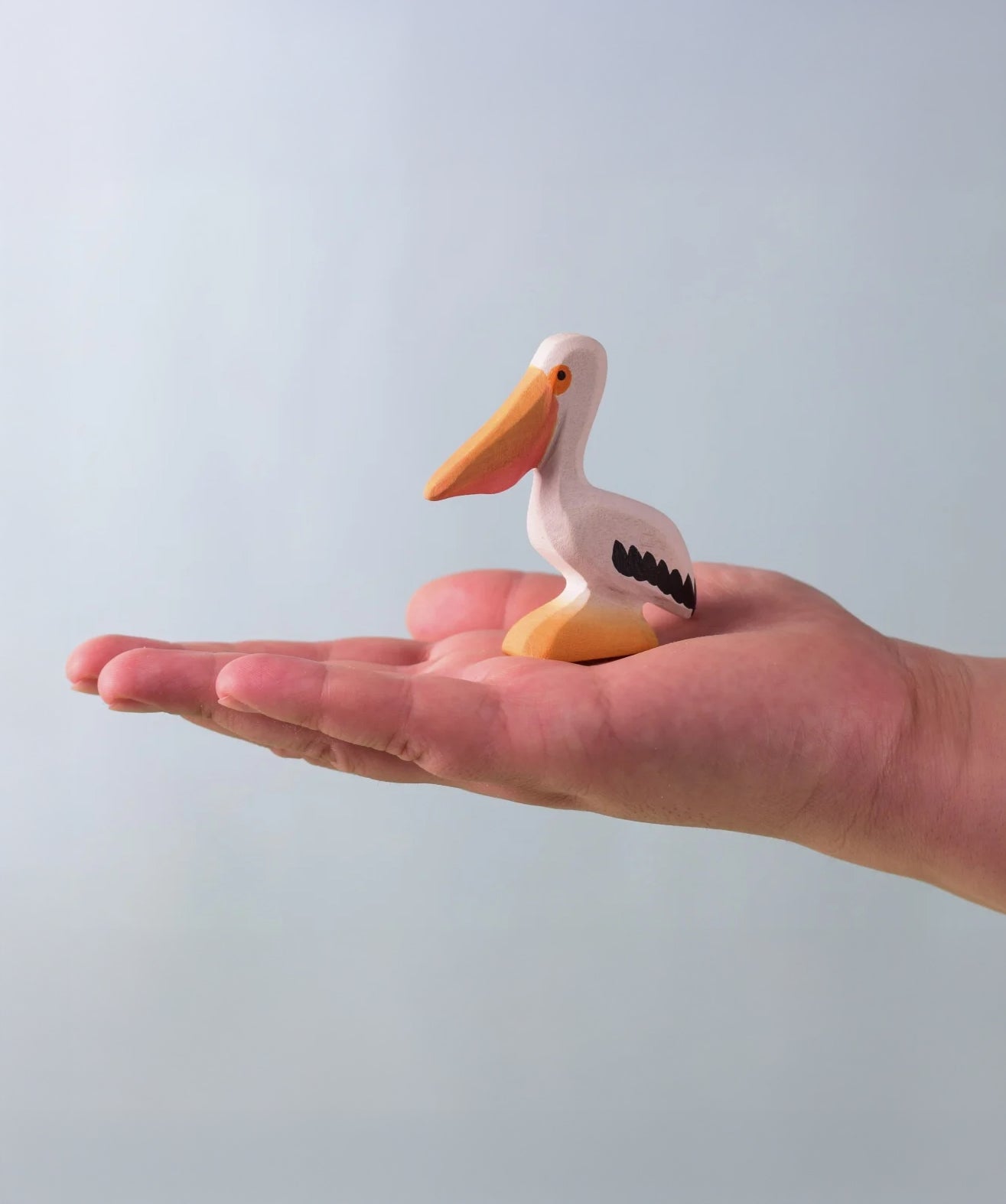Bumbu Toys Wooden Pelican, being held in an adult's hand.
