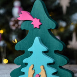 A Bumbu Christmas Tree Nativity Puzzle in a Fuchsia colour way in front of a Christmas tree. 