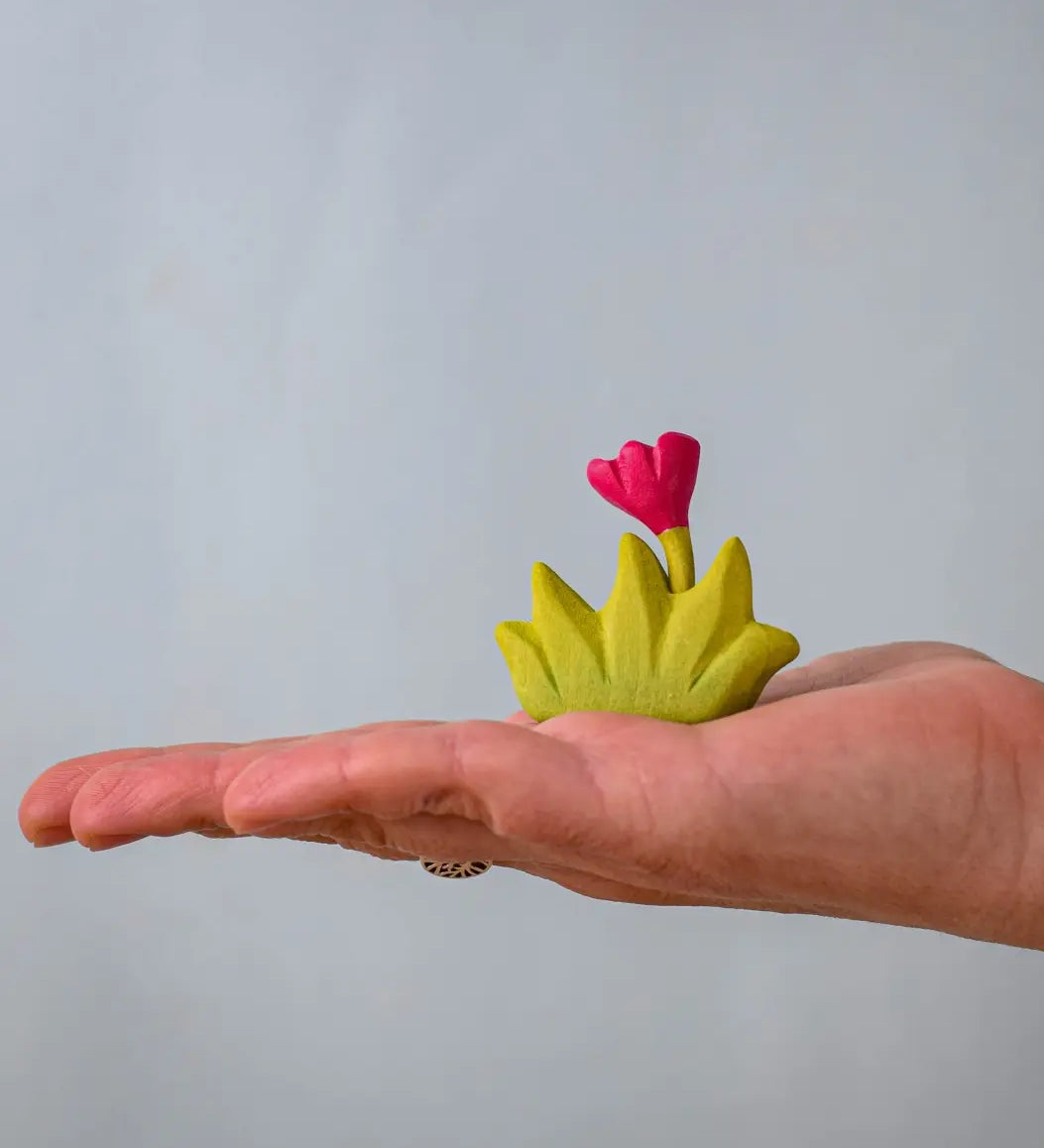 Bumbu small wooden grass with pink flower for use as scenery in small world play on an adult's hand.