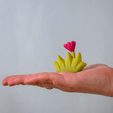 Bumbu small wooden grass with pink flower for use as scenery in small world play on an adult's hand.