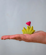 Bumbu small wooden grass with pink flower for use as scenery in small world play on an adult's hand.