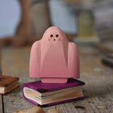 A Bumbu pink ghost figure placed on a wooden book. These expertly hand crafted items are part of a large range of wooden toys available here at Babipur. 