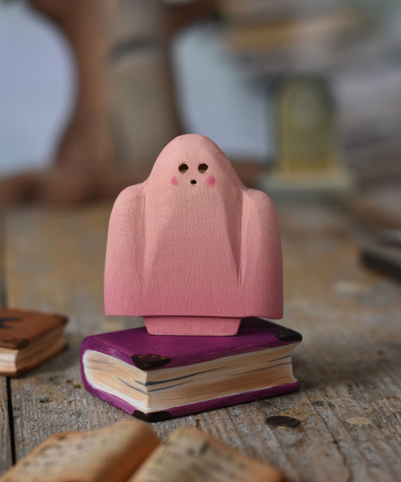 A Bumbu pink ghost figure placed on a wooden book. These expertly hand crafted items are part of a large range of wooden toys available here at Babipur. 