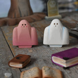 A pink and white Bumbu ghost placed on a wooden surface in a small world play scene. There are little wooden books in front of them and a spooky tree and a gravestone in the background. These expertly hand crafted items are part of a large range of wooden toys available here at Babipur. 