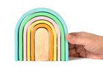 Close up of a hand holding the Bumbu eco-friendly stacking pastel arches on a white background