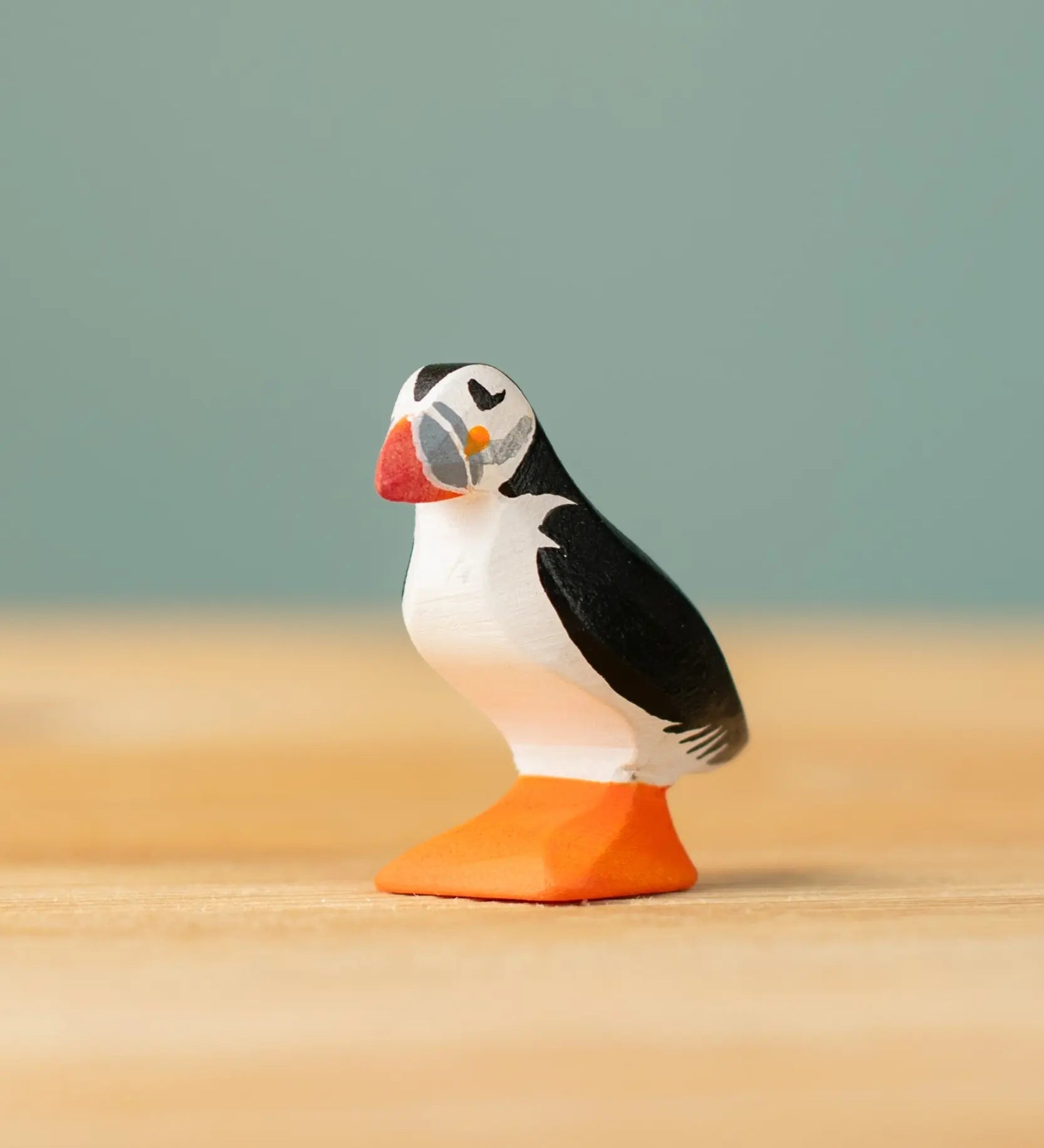 Bumbu Toys puffin handmade wooden toy figure placed on a wooden surface. 