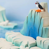 Bumbu Toys puffin handmade wooden toy figure placed on an ice berg wooden scenery piece.