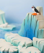 Bumbu Toys puffin handmade wooden toy figure placed on an ice berg wooden scenery piece.