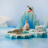 Bumbu Toys puffin handmade wooden toy figure placed on an ince berg scenery piece with harp seals and pup.