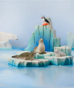 Bumbu Toys puffin handmade wooden toy figure placed on an ince berg scenery piece with harp seals and pup.