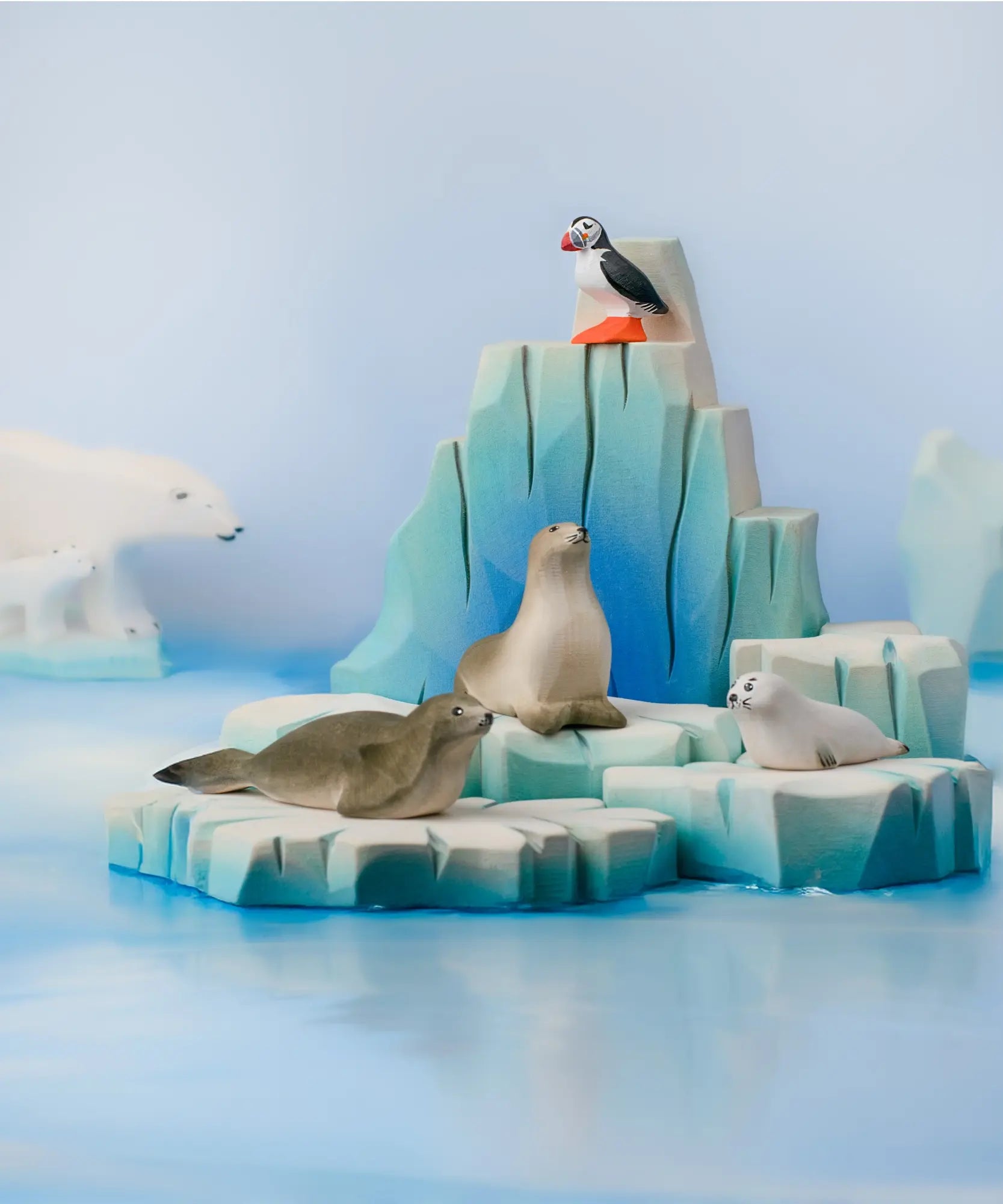 Bumbu Toys puffin handmade wooden toy figure placed on an ince berg scenery piece with harp seals and pup.
