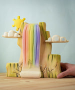 A hand reaching in to hold the Bumbu Toys Rainbow Cliff placed on a wooden surface.