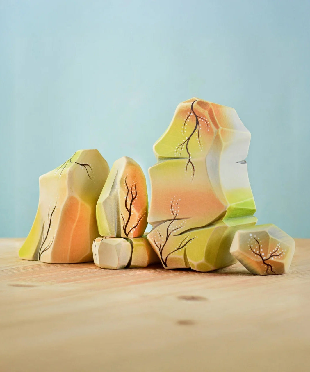The Bumbu Toys Rainbow Rocks are wooden figures hand painted with green, orange background and brown and white coloured detailing. 