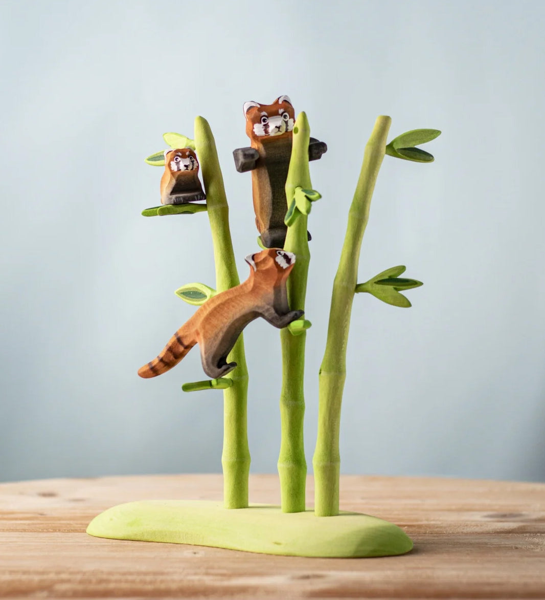 A nature play scene featuring the playful, cub and standing red panda balancing on the Bumbu bamboo. 