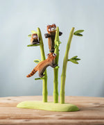 A nature play scene featuring the playful, cub and standing red panda balancing on the Bumbu bamboo. 