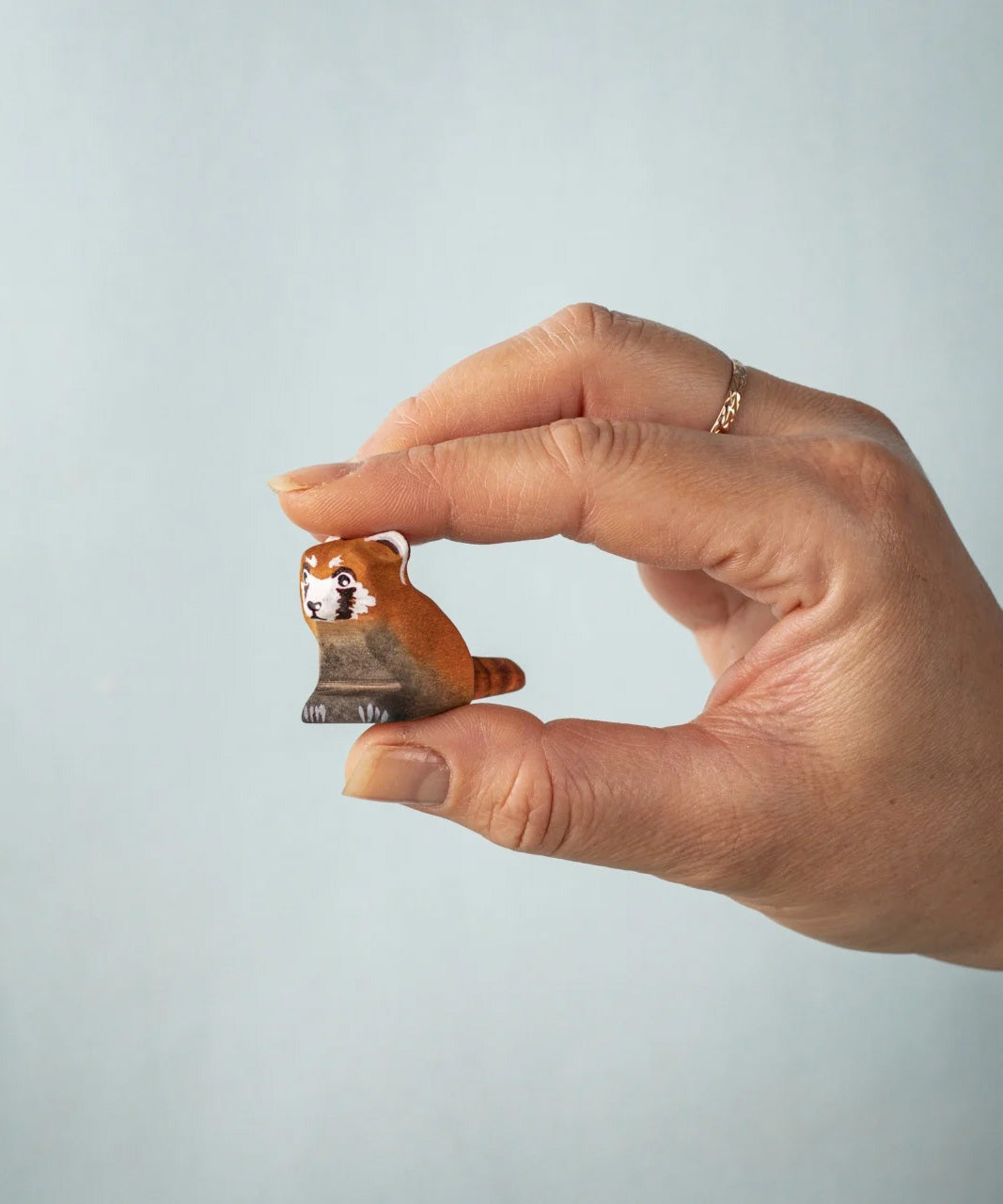 A hand holding the Bumbu wooden red panda cub