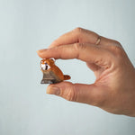 A hand holding the Bumbu wooden red panda cub