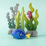 The Bumbu Royal Blue Tang fish wooden toy, in a play scene with seaweed and a seahorse