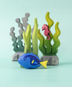 The Bumbu Royal Blue Tang fish wooden toy, in a play scene with seaweed and a seahorse
