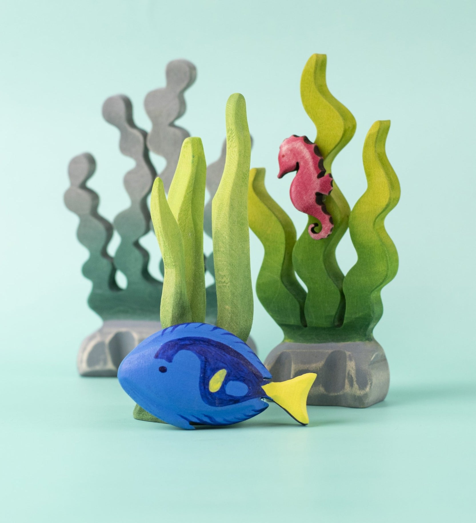 The Bumbu Royal Blue Tang fish wooden toy, in a play scene with seaweed and a seahorse