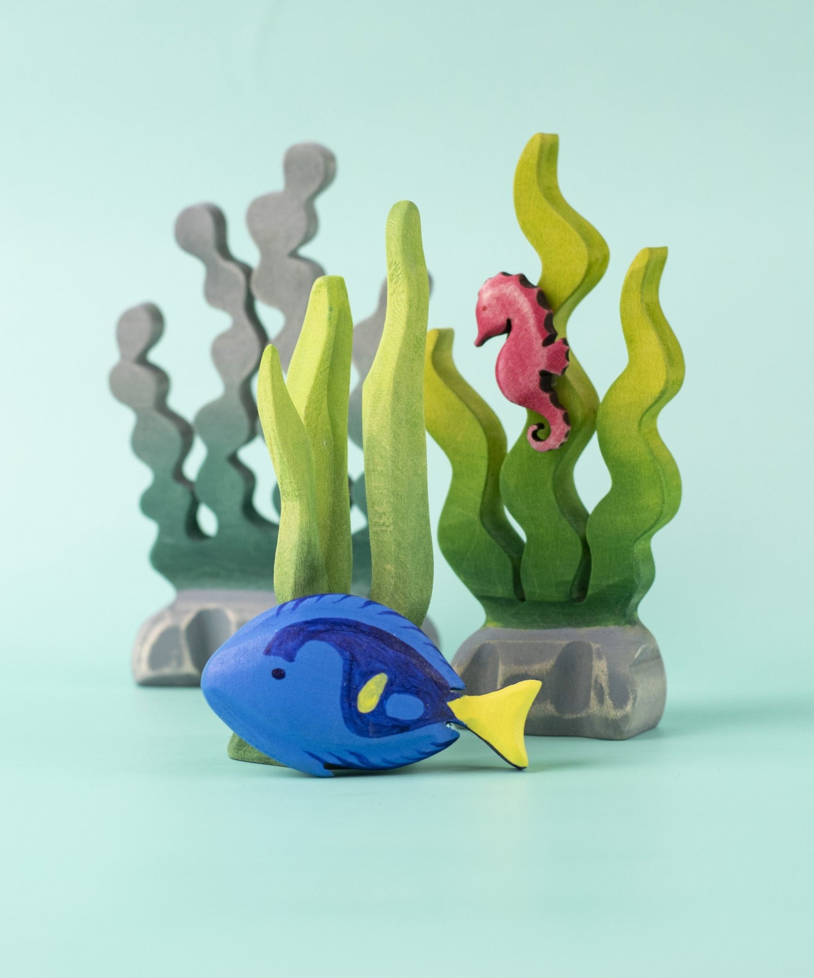 The Bumbu Royal Blue Tang fish wooden toy, in a play scene with seaweed and a seahorse