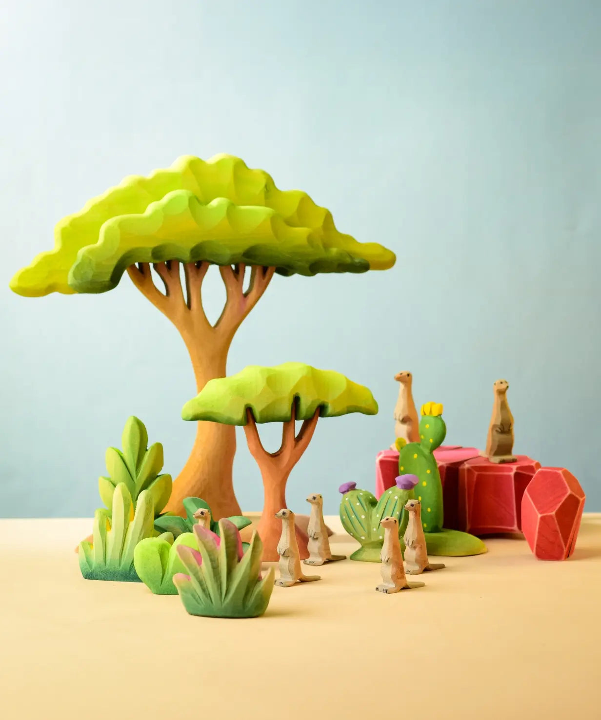 Bumbu Toys savanna bush wooden toy scenery figure placed at the front of a small world play scene with meercats, rocks and trees in the back.