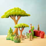 Bumbu Toys savanna bush wooden toy scenery figure placed at the front of a small world play scene with meercats, rocks and trees in the back.