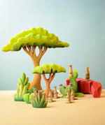 Bumbu Toys savanna bush wooden toy scenery figure placed at the front of a small world play scene with meercats, rocks and trees in the back.