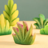 Bumbu Toys savanna bush wooden toy scenery figure placed on a wooden surface with other bushes in the background. 