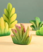 Bumbu Toys savanna bush wooden toy scenery figure placed on a wooden surface with other bushes in the background. 