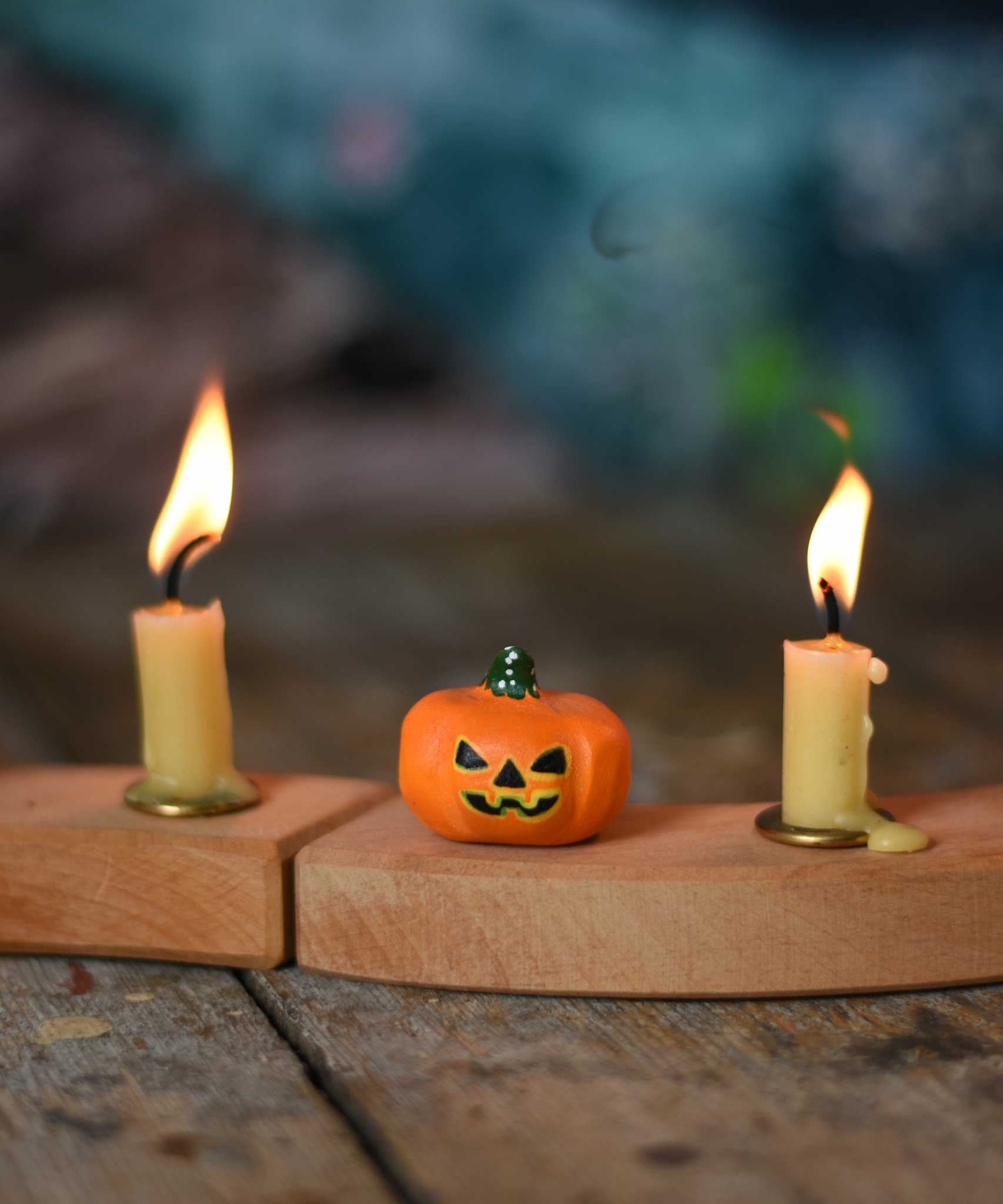 A small Bumbu Halloween figure placed on a wooden Grimm's celebration ring in between to lit candles.