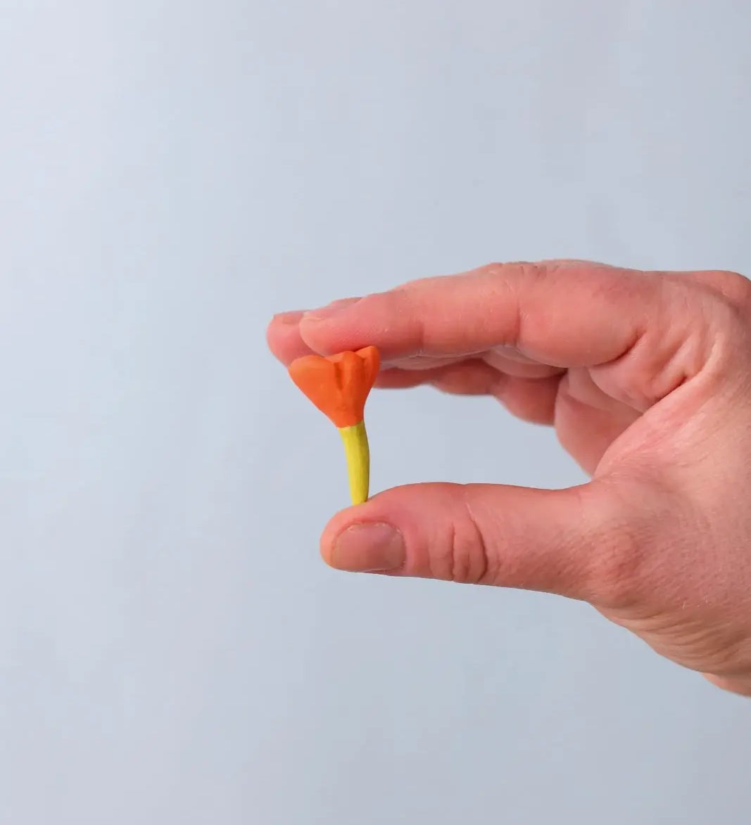 Bumbu Toys small wooden flower in orange in an adult's hand.