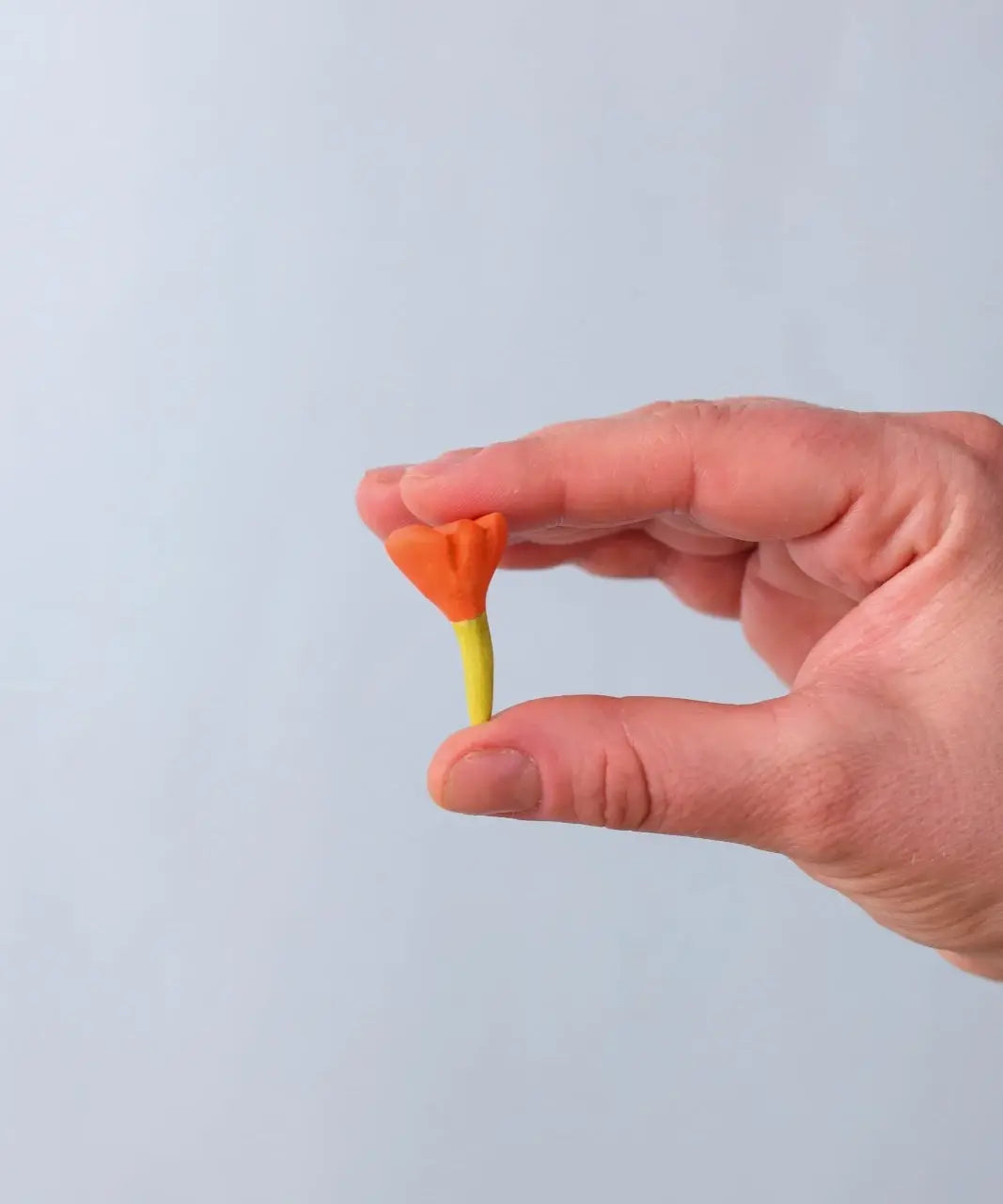 Bumbu Toys small wooden flower in orange in an adult's hand.