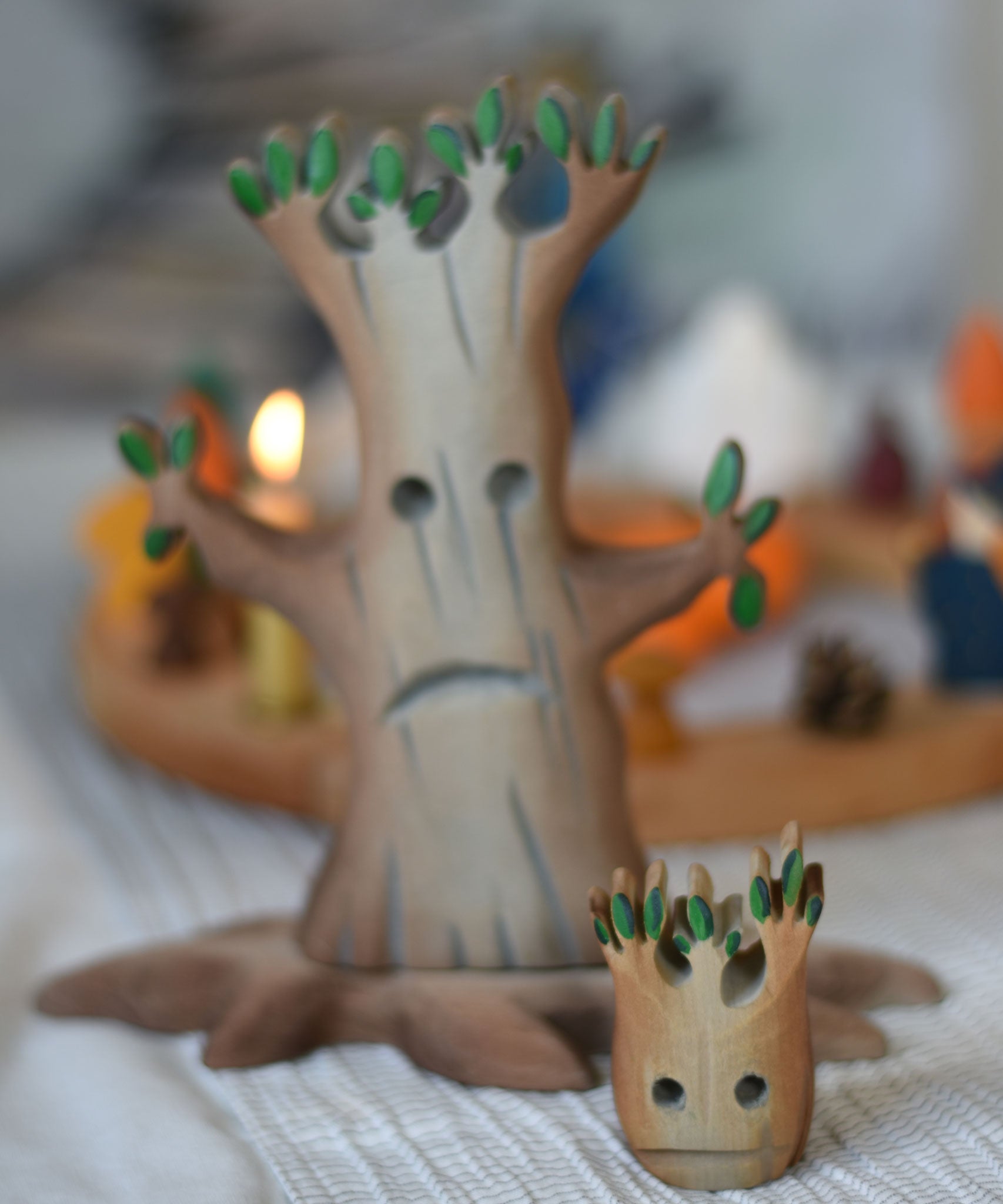 A small Bumbu spooky tree figure placed on a light grey tablecloth, a large tree and celebration ring can be seen blurred out in the background.