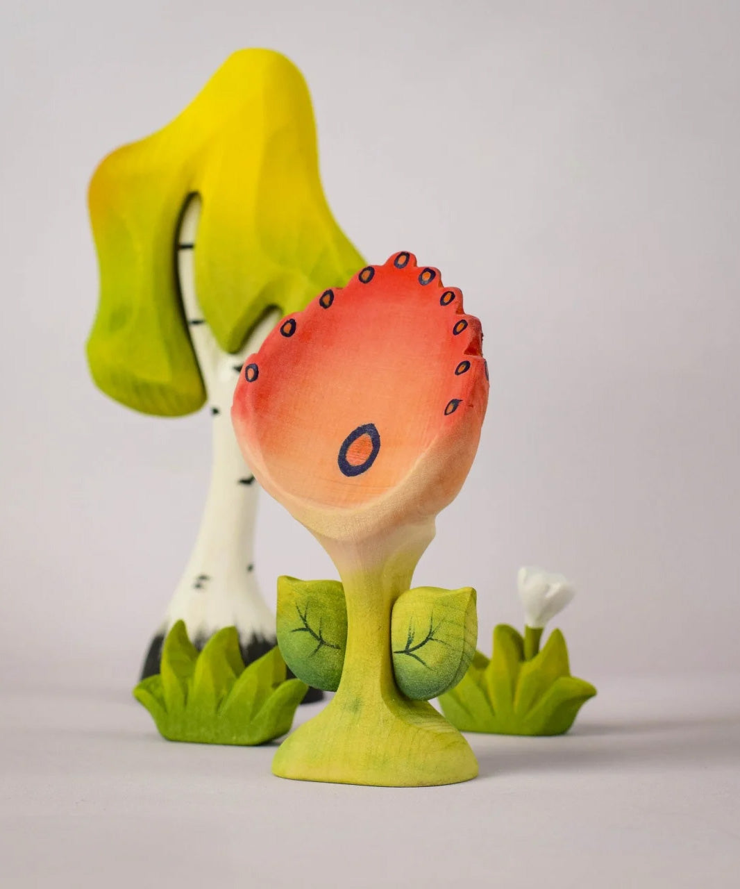 The Bumbu Toys Perla Spring Flower shown in front of a Bumbu tree and white flower. 