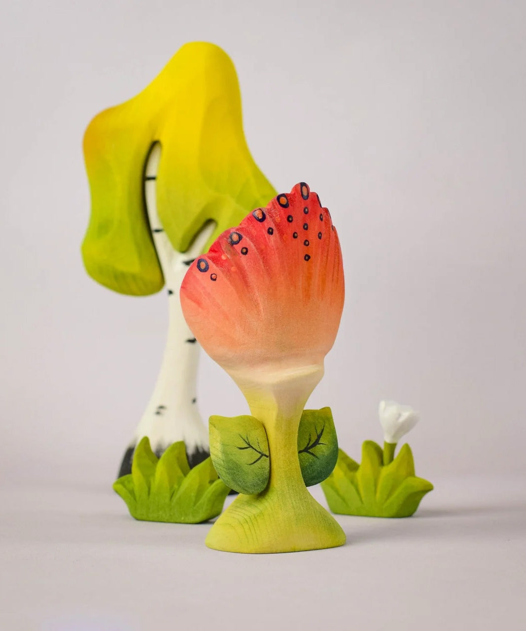 The front of a Bumbu Toys Perla Spring Flower shown in front of a Bumbu tree and white flower. 