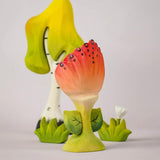 The front of a Bumbu Toys Perla Spring Flower shown in front of a Bumbu tree and white flower. 