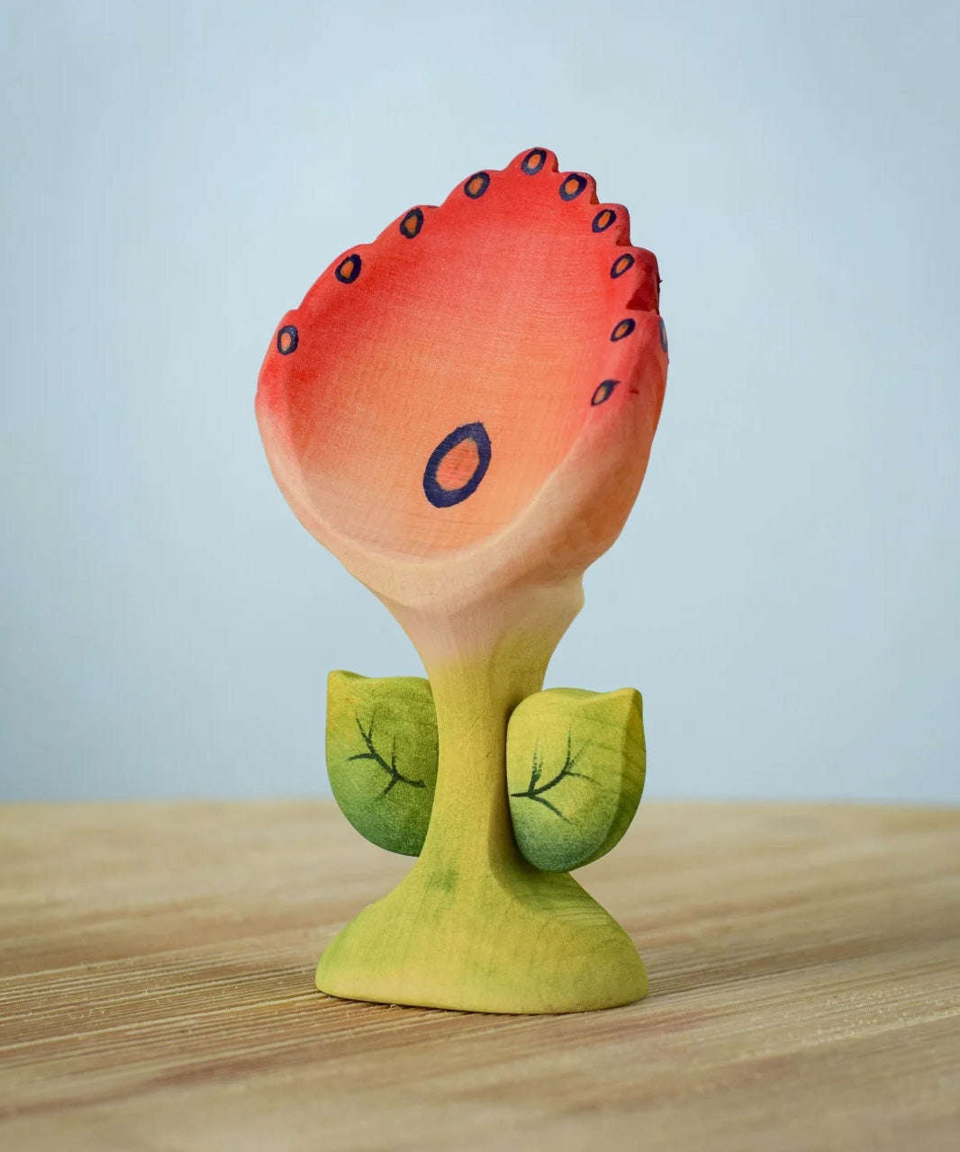 The Bumbu Toys Perla Spring Flower has a red flower with blue detailing and a green coloured stem. 
