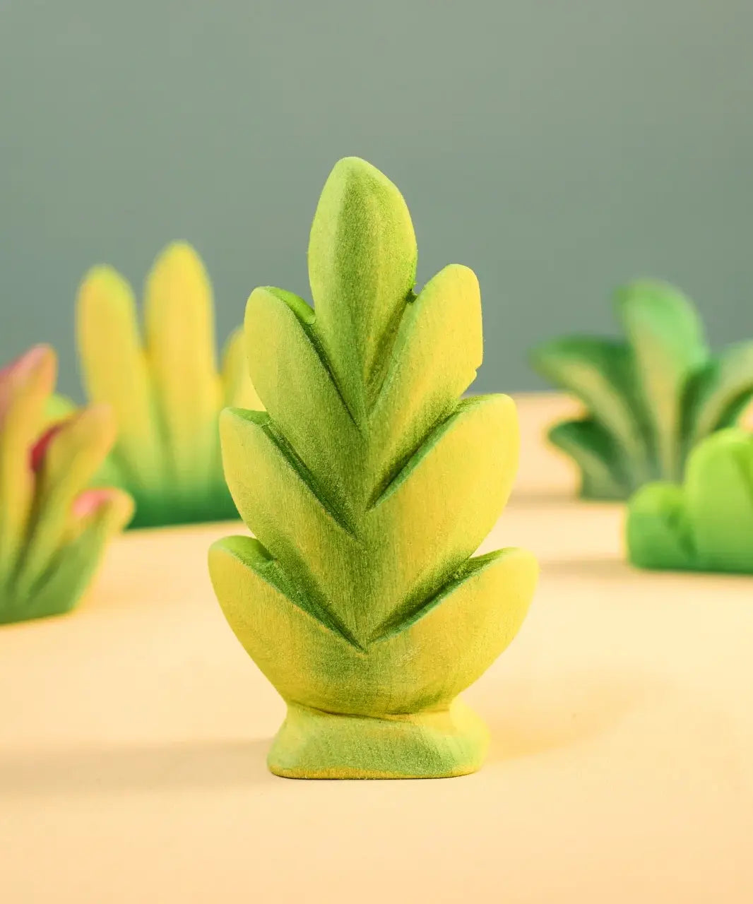 Bumbu Toys thuja shrub wooden toy scenery piece placed on a wooden surface with other bushes and shrub pieces in the background.