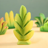 Bumbu Toys thuja shrub wooden toy scenery piece placed on a wooden surface with other bushes and shrub pieces in the background.
