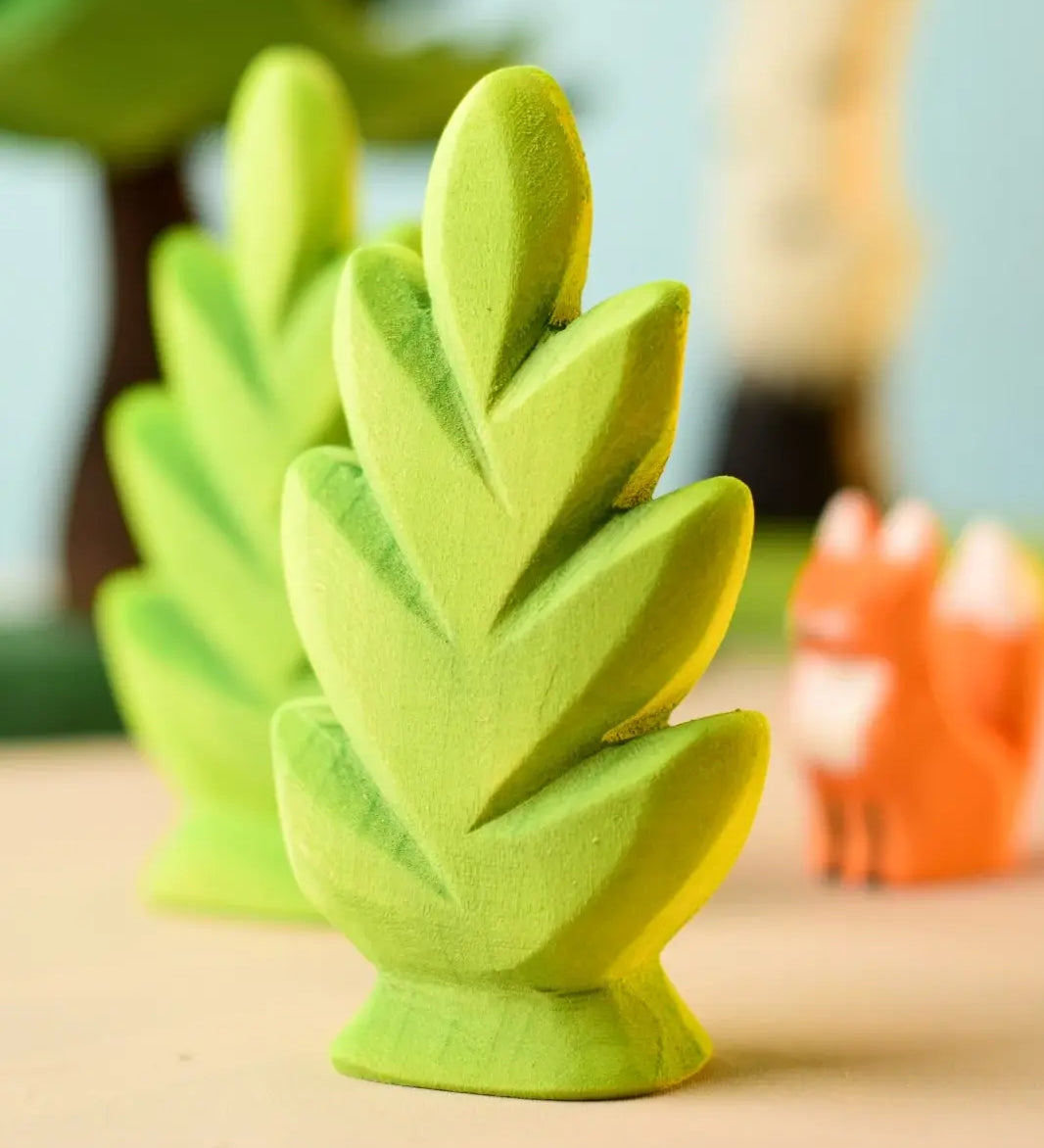 Bumbu Toys thuja shrub wooden toy scenery piece placed on a wooden surface with other toys blurred in the background.