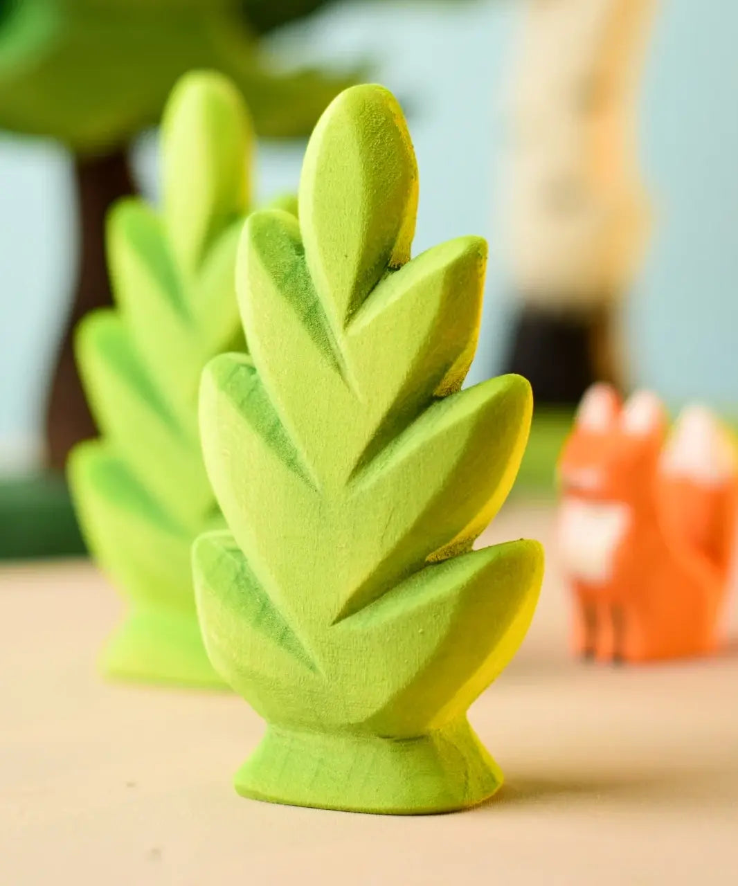 Bumbu Toys thuja shrub wooden toy scenery piece placed on a wooden surface with other toys blurred in the background.