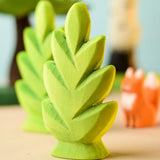 Bumbu Toys thuja shrub wooden toy scenery piece placed on a wooden surface with other toys blurred in the background.