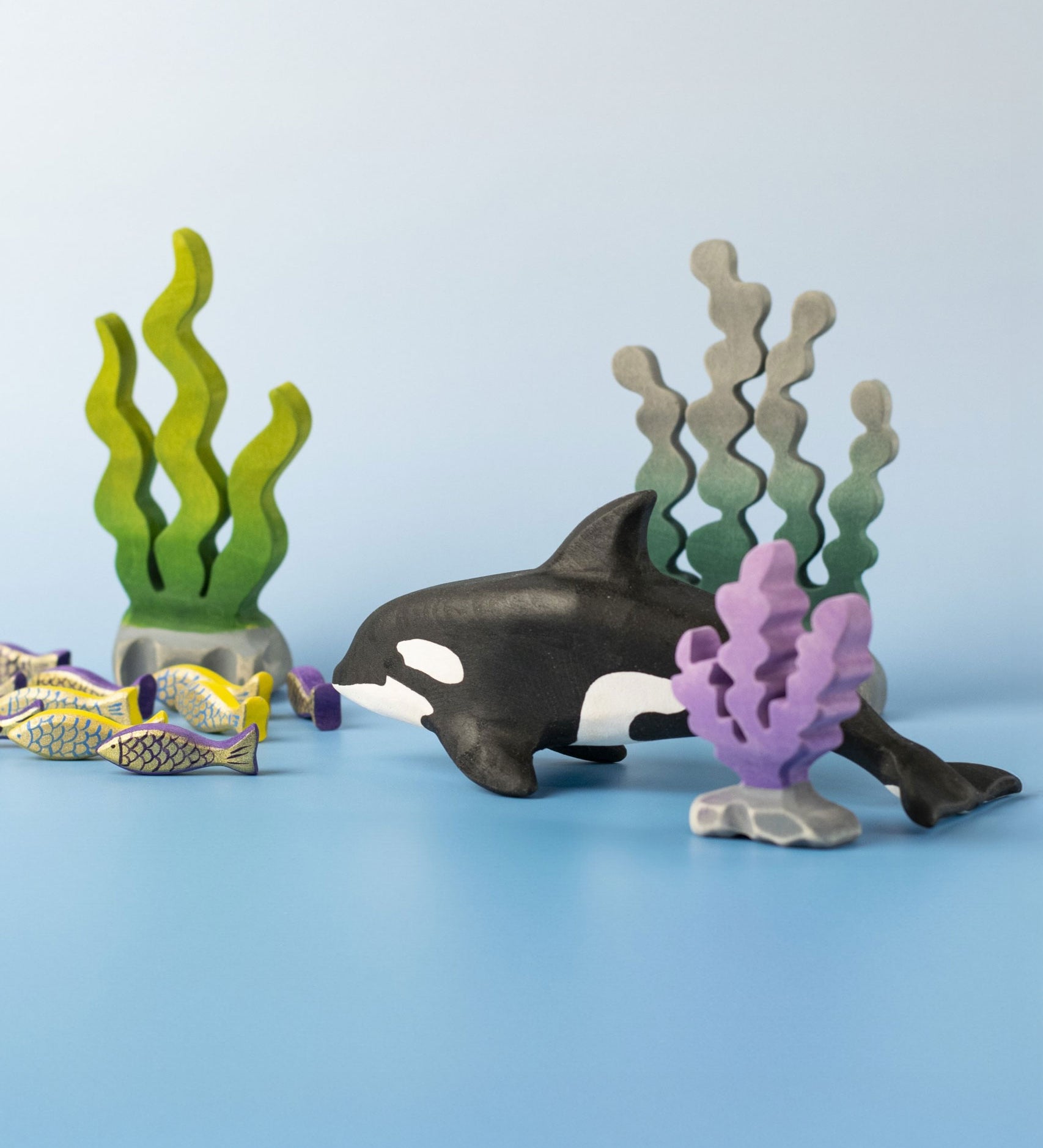 A Bumbu Toys Orca handmade wooden toy figure placed in the centre of a underwater themed small world play scene. The Orca whale is part of a large range of handmade wooden toys here at Babipur.