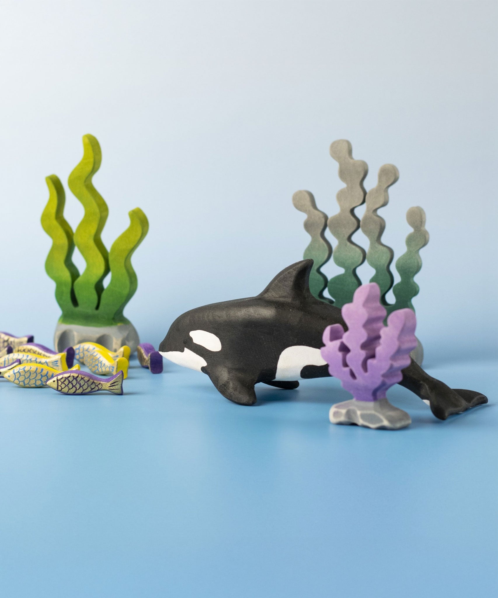 A Bumbu Toys Orca handmade wooden toy figure placed in the centre of a underwater themed small world play scene. The Orca whale is part of a large range of handmade wooden toys here at Babipur.