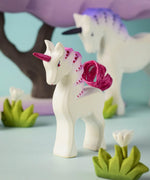 A close up of a Bumbu Toys Pastel Baby Unicorn wooden figure in a small world play scene. 
