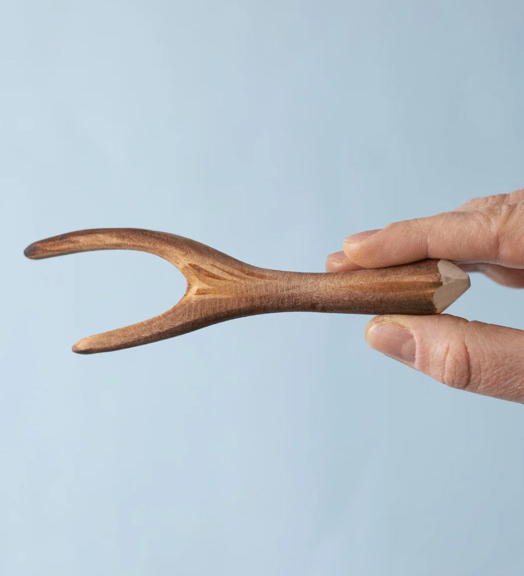 An adult's hand holding up a Bumbu Toys Black Poplar Branch.