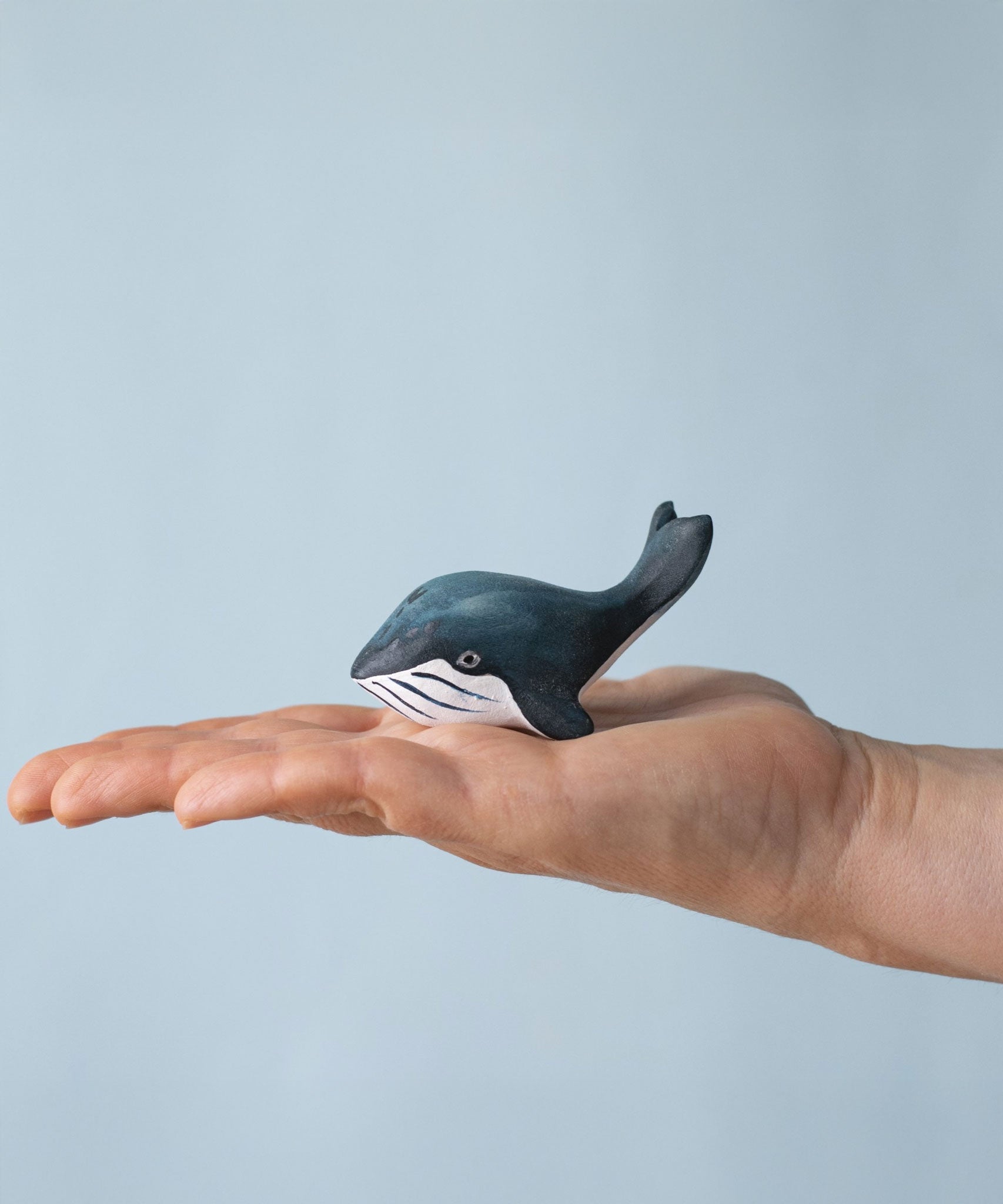 A Bumbu Toys Baby Blue Whale placed on the palm of an adult's hand to show scale. 