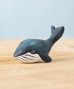 A Bumbu Toys Baby Blue Whale placed on a wooden surface. We have a wide range of Bumbu handmade wooden figures here at Babipur.
